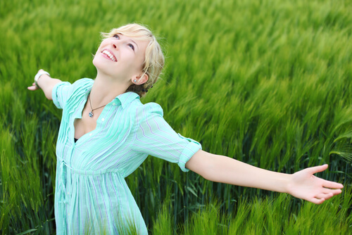 Szczęśliwa kobieta rozkłąda rece na zielonej trawie
