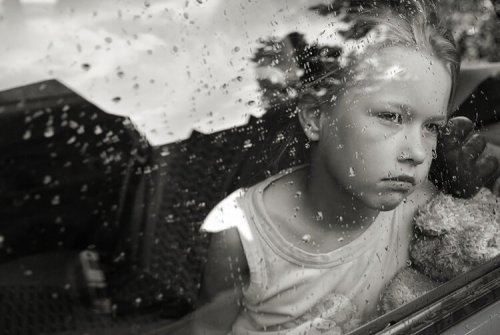 Mała dziewczynka smutno patrzy przez okno