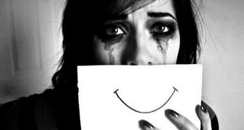 Płacząca kobieta zakrywa twarz kartką z uśmiechem