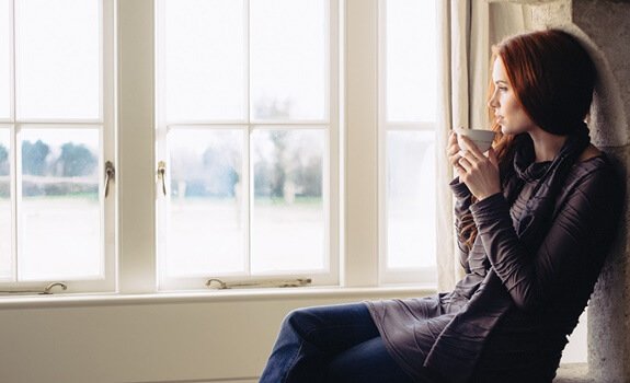 Kobieta z kawą przy oknie.