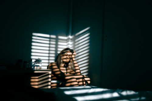 Nadużycia - zmartwiona kobieta siedzi w ciemnym pokoju