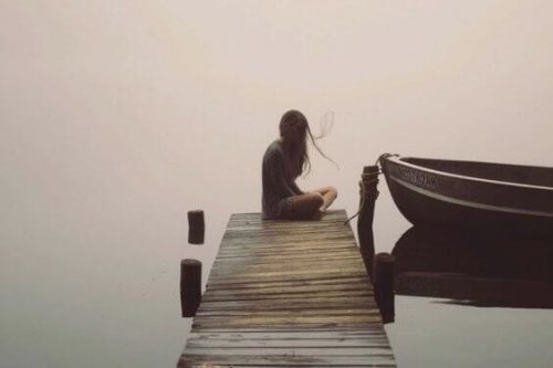 samotna kobieta siedzi na molo nad jeziorem