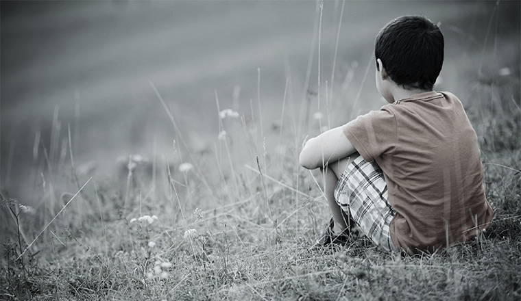 Smutny chłopczyk siedzi na trawie