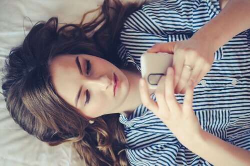 Dziewczyna leżąca na łóżku z telefonem w dłoniach - czy to uzależnienie od WhatsApp?