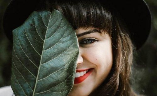 Kobieta ukrywa za liściem pół twarzy z uśmiechem Duchenn'a
