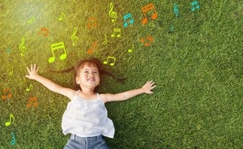 Dziecko leży na trawie i ogląda kolorowe nuty - wpływ muzykoterapii