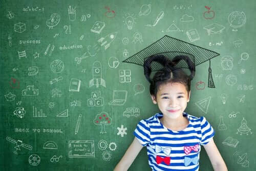 Dziewczynka uczy się przy zielonej tablicy szkolnej i czapką absolwenta