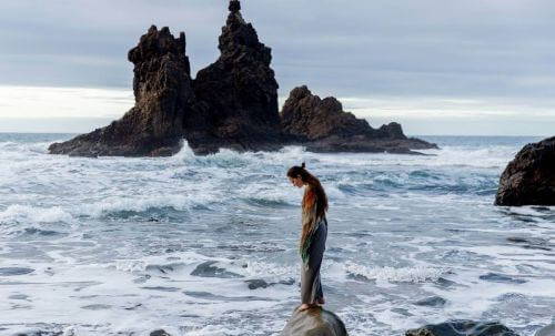 Kobieta stoi ze spuszczoną głową na skale na wzburzonym morzu