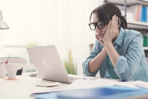 Znudzona kobieta w okularach podbiera głowę na rękach i myśli przed komputerem