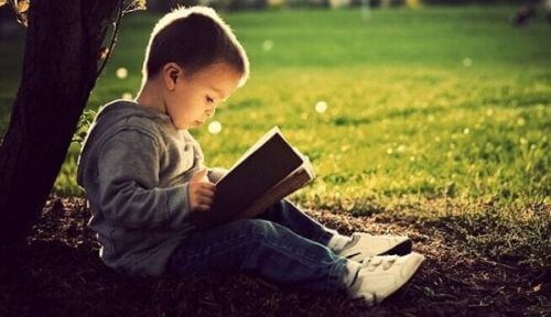 Male dziecko czyta grubą książkę, siedząc pod drzewem