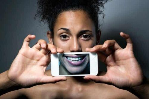 Kobieta zakrywa sobie twarz sztucznym uśmiechem na ekranie telefonu